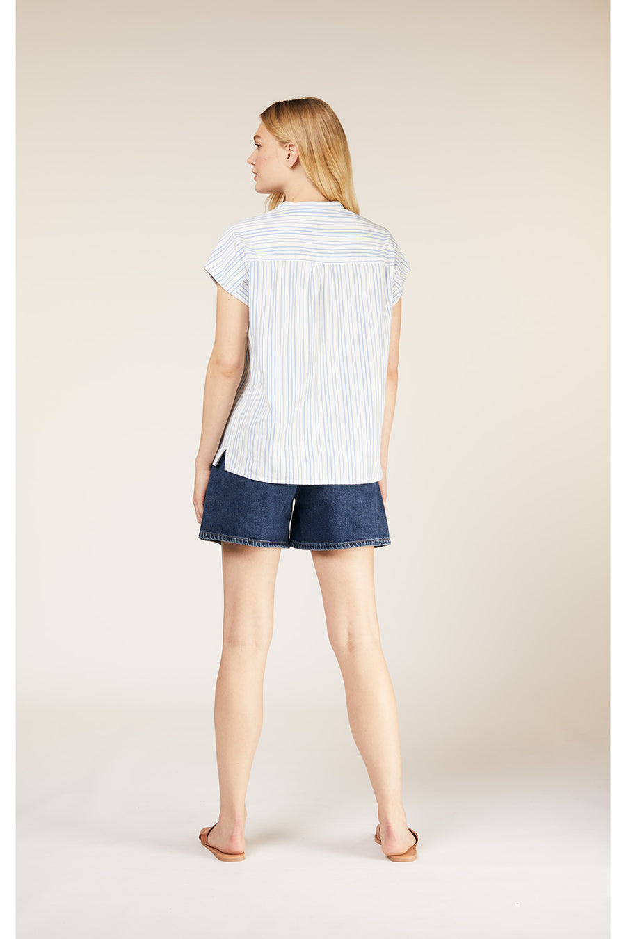 A standing shot of a model showing the back of a striped handwoven top untucked. 